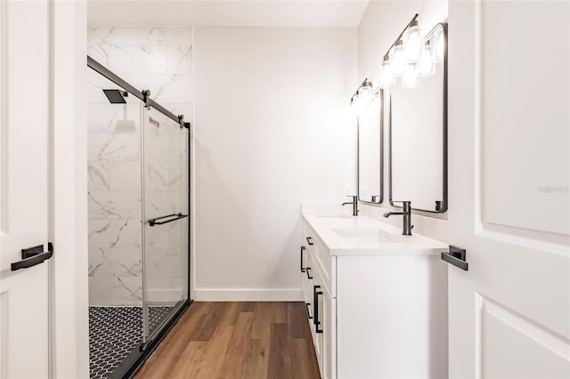 bathroom featuring a marble finish shower, baseboards, double vanity, wood finished floors, and a sink