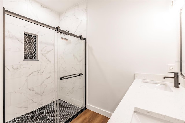 full bathroom featuring wood finished floors, baseboards, a marble finish shower, and a sink