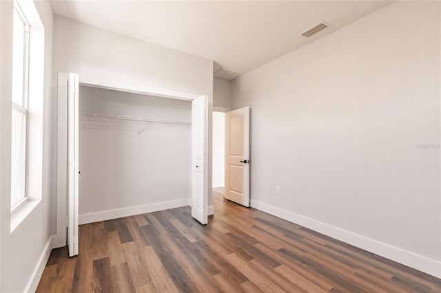 unfurnished bedroom featuring dark wood-type flooring, baseboards, visible vents, and a closet