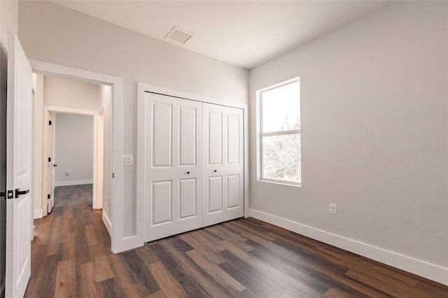 unfurnished bedroom featuring dark wood-type flooring, baseboards, visible vents, and a closet