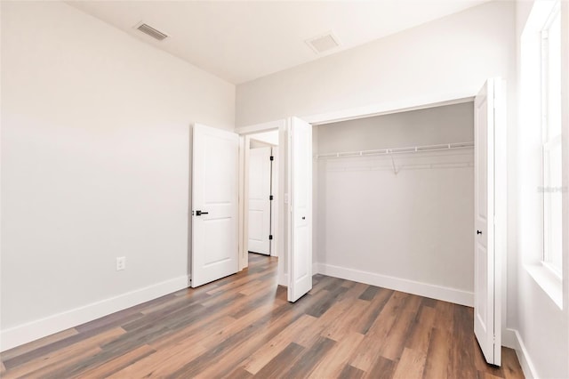 unfurnished bedroom with wood finished floors, visible vents, a closet, and baseboards