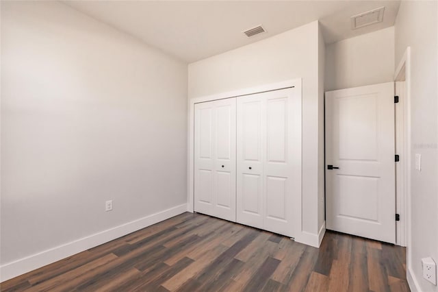 unfurnished bedroom with dark wood-style floors, visible vents, a closet, and baseboards