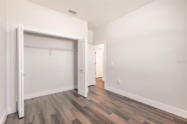 unfurnished bedroom with dark wood-style floors, visible vents, a closet, and baseboards