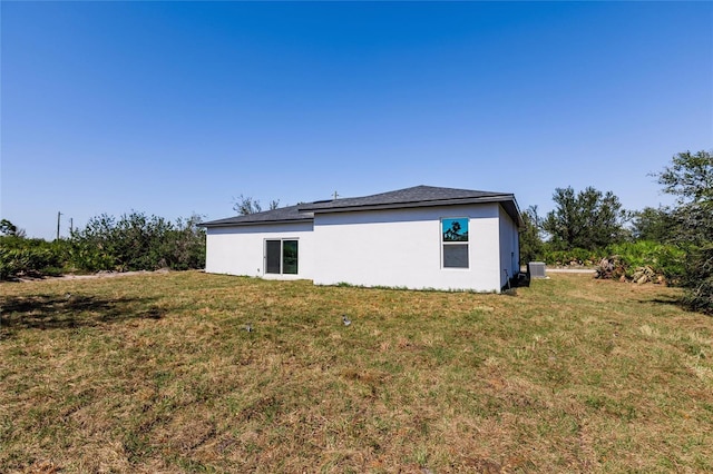 view of side of property with stucco siding, a yard, and cooling unit