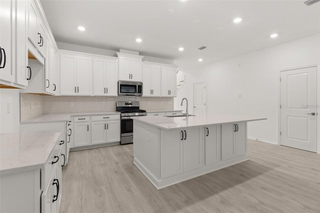 kitchen featuring a sink, decorative backsplash, light wood-style flooring, stainless steel appliances, and a kitchen island with sink