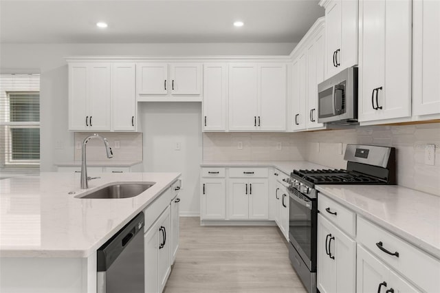 kitchen with a sink, appliances with stainless steel finishes, a kitchen island with sink, and white cabinetry