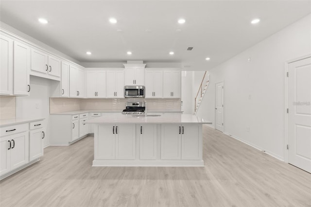 kitchen with light countertops, light wood-style flooring, a center island with sink, and stainless steel appliances