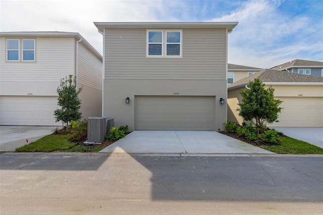 traditional-style house with concrete driveway, central AC unit, a garage, and stucco siding