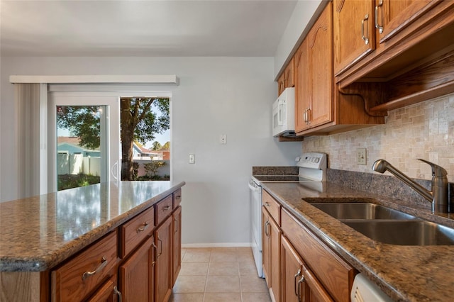 kitchen with backsplash, dark stone countertops, brown cabinets, white appliances, and a sink