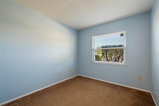 spare room featuring baseboards, dark carpet, and a textured ceiling