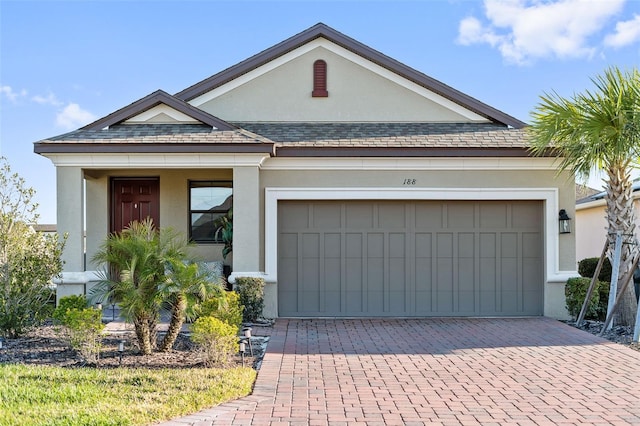 view of front of home with stucco siding, decorative driveway, a garage, and a shingled roof