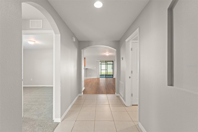 hallway with visible vents, baseboards, light carpet, light tile patterned floors, and arched walkways