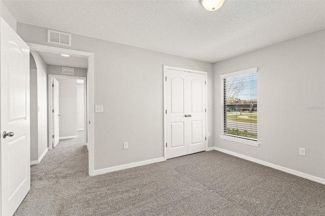 unfurnished bedroom with visible vents, carpet floors, a textured ceiling, and baseboards