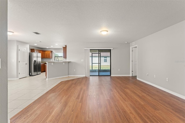 unfurnished living room with a sink, visible vents, baseboards, and a textured ceiling