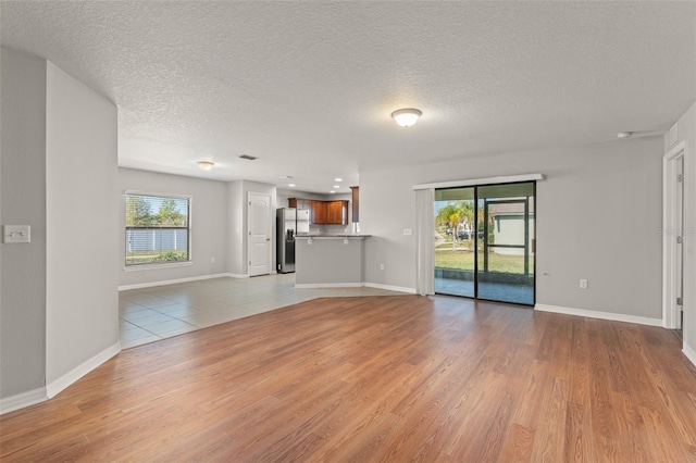 unfurnished living room featuring light wood-style flooring, plenty of natural light, baseboards, and a textured ceiling