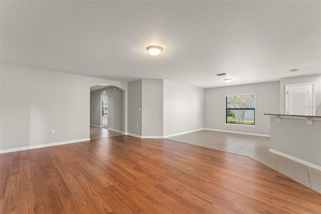 unfurnished living room with visible vents, baseboards, arched walkways, a textured ceiling, and tile patterned floors