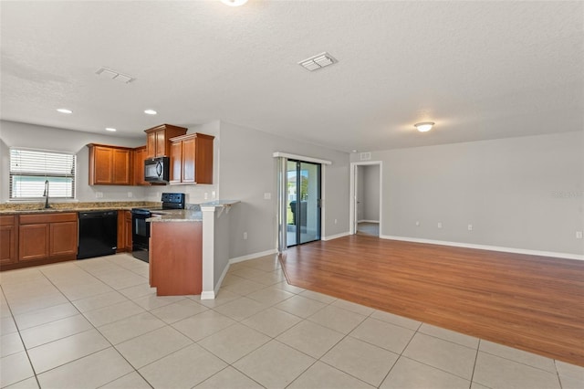 kitchen with light tile patterned floors, open floor plan, brown cabinets, and black appliances