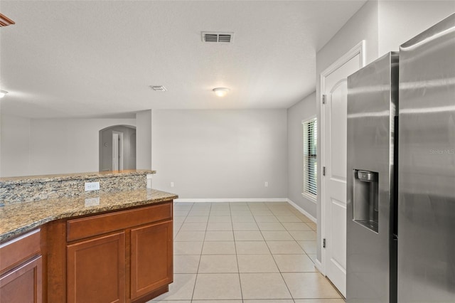 kitchen with visible vents, brown cabinets, stainless steel refrigerator with ice dispenser, arched walkways, and light tile patterned floors