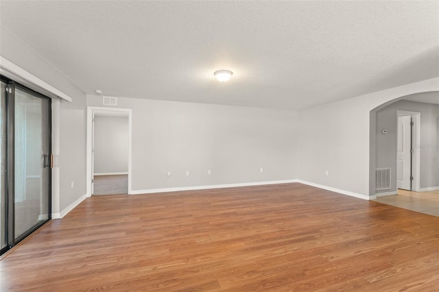 empty room featuring light wood-type flooring, visible vents, and arched walkways