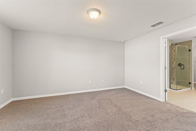 empty room with visible vents, light colored carpet, a textured ceiling, and baseboards