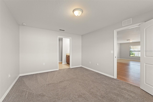 unfurnished room featuring baseboards, light colored carpet, visible vents, and a textured ceiling