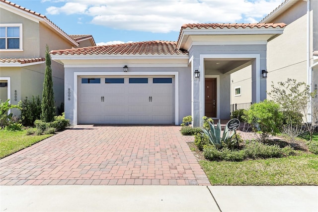 view of front of property featuring stucco siding, an attached garage, a tile roof, and decorative driveway