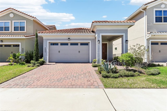 mediterranean / spanish-style house with a tiled roof, decorative driveway, an attached garage, and stucco siding