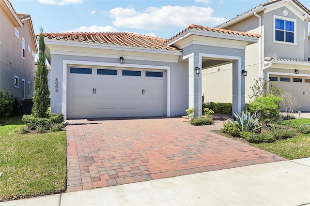 mediterranean / spanish-style house featuring stucco siding, decorative driveway, a garage, and a tiled roof