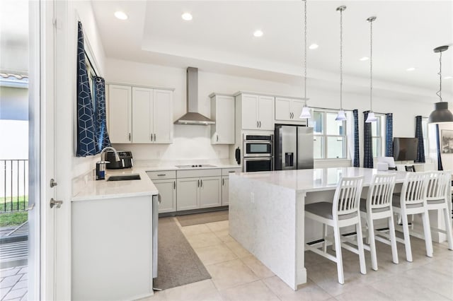 kitchen with a center island, wall chimney range hood, light countertops, stainless steel appliances, and a sink