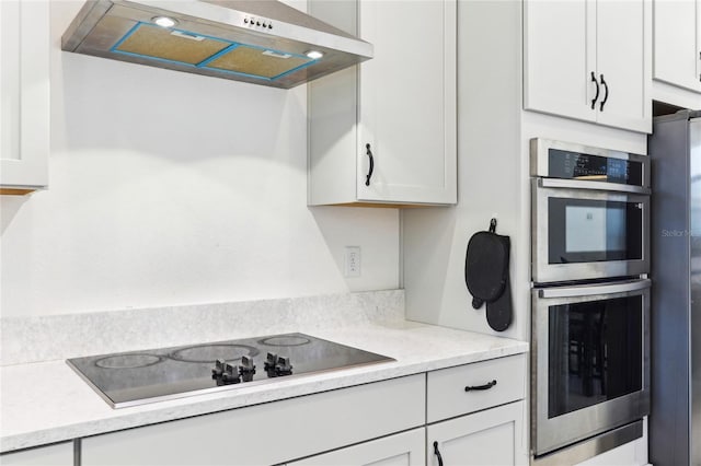 kitchen featuring stainless steel appliances, white cabinetry, light countertops, and wall chimney range hood