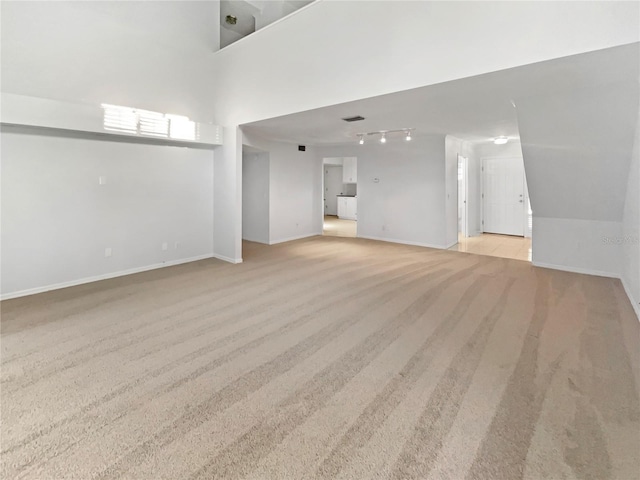 unfurnished living room with rail lighting, light colored carpet, and baseboards