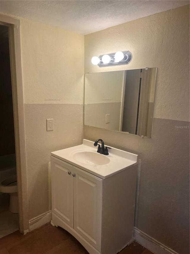 bathroom with toilet, a textured ceiling, baseboards, vanity, and a textured wall