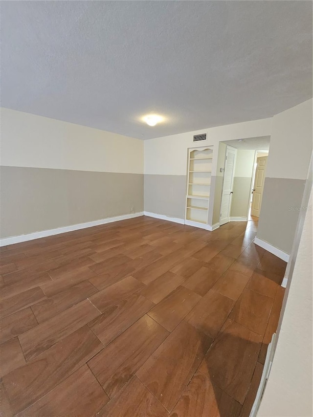 unfurnished room featuring wood finished floors, visible vents, and a textured ceiling