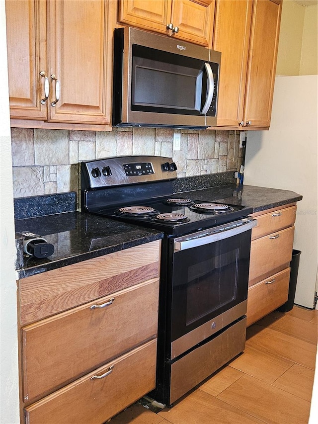 kitchen featuring backsplash, dark stone counters, light wood-style floors, and appliances with stainless steel finishes