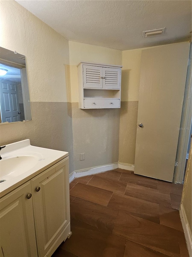 bathroom with visible vents, a textured ceiling, wood finished floors, and a textured wall