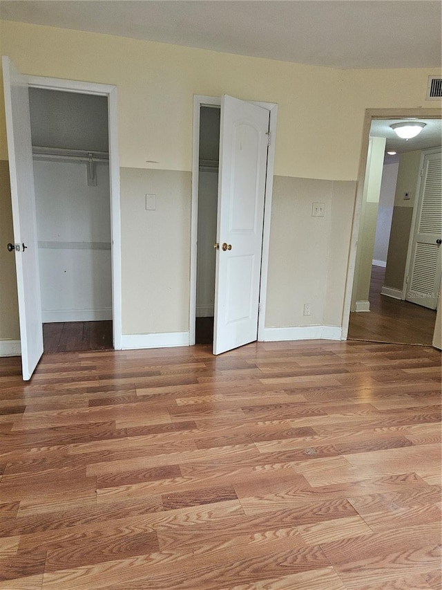 unfurnished bedroom featuring visible vents, baseboards, two closets, and light wood-style flooring