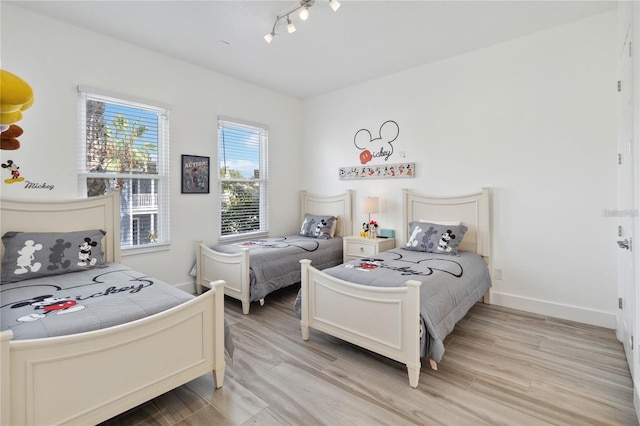 bedroom featuring track lighting, light wood-style flooring, and baseboards