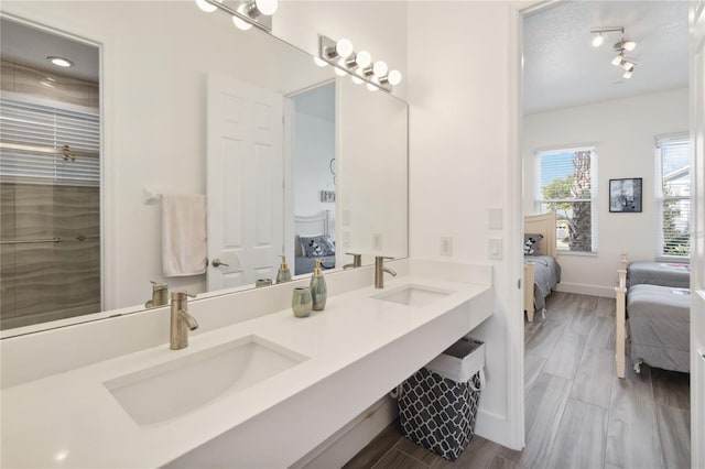 ensuite bathroom featuring a sink, connected bathroom, baseboards, and wood finished floors