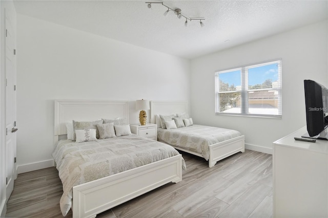 bedroom with a textured ceiling, baseboards, and wood finished floors