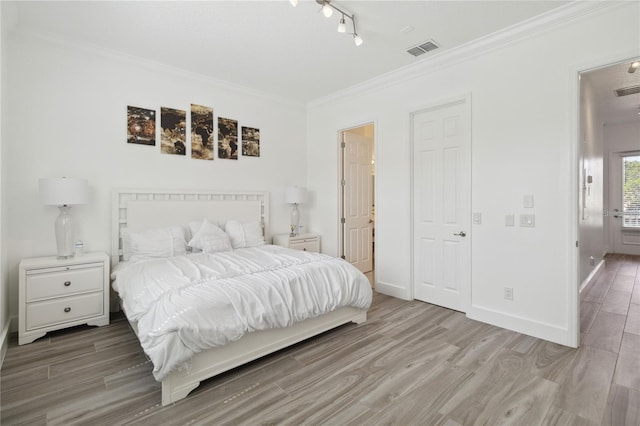 bedroom featuring baseboards, wood finished floors, visible vents, and ornamental molding