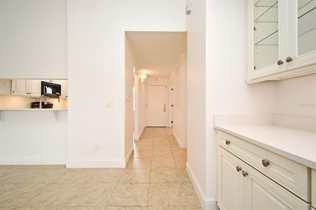 interior space featuring baseboards, light countertops, glass insert cabinets, black microwave, and white cabinetry