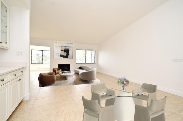 dining room featuring light tile patterned floors, a fireplace, baseboards, and lofted ceiling