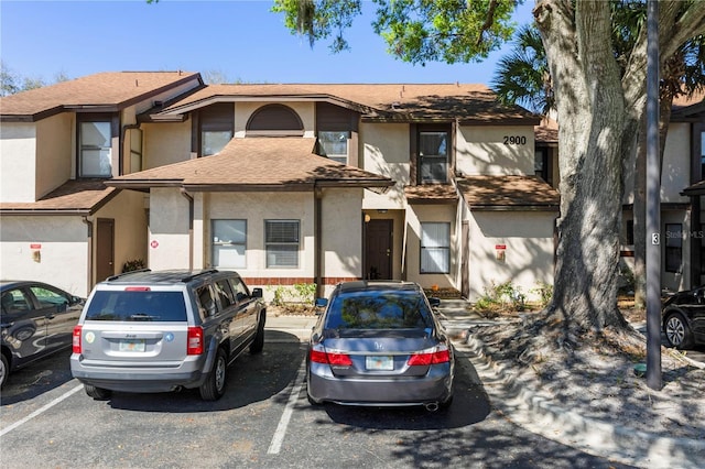 view of property with a shingled roof, uncovered parking, and stucco siding