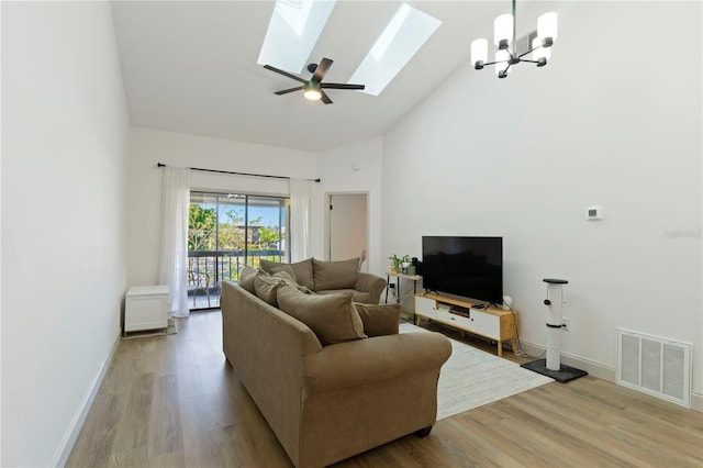 living area featuring light wood finished floors, visible vents, a skylight, a notable chandelier, and high vaulted ceiling