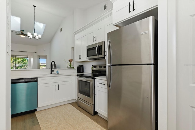 kitchen featuring lofted ceiling with skylight, a sink, white cabinetry, appliances with stainless steel finishes, and light countertops