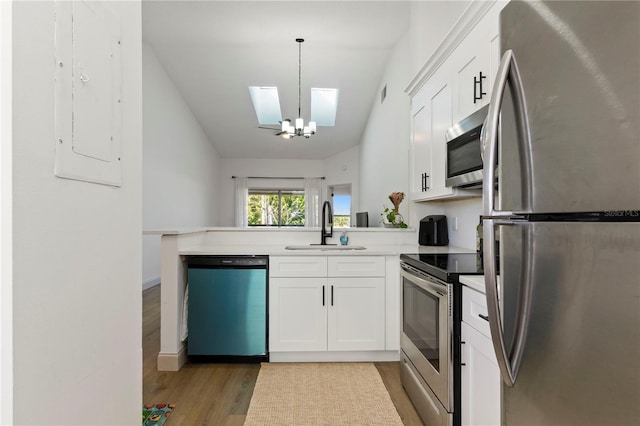 kitchen with a sink, white cabinetry, stainless steel appliances, a peninsula, and light wood finished floors