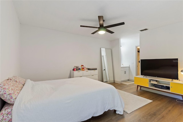 bedroom featuring a ceiling fan, wood finished floors, visible vents, baseboards, and ensuite bathroom