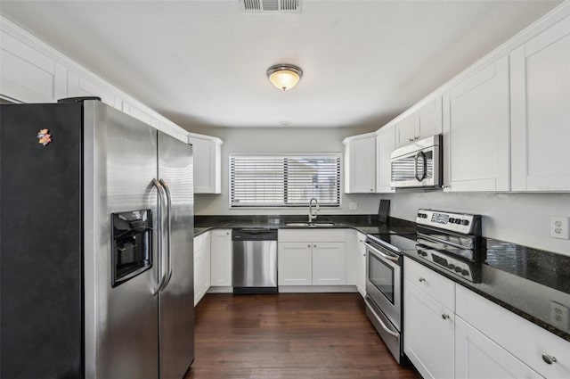 kitchen with a sink, dark countertops, dark wood-style floors, appliances with stainless steel finishes, and white cabinets