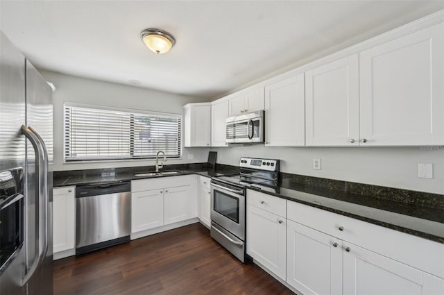 kitchen featuring a sink, dark stone counters, appliances with stainless steel finishes, white cabinetry, and dark wood-style flooring