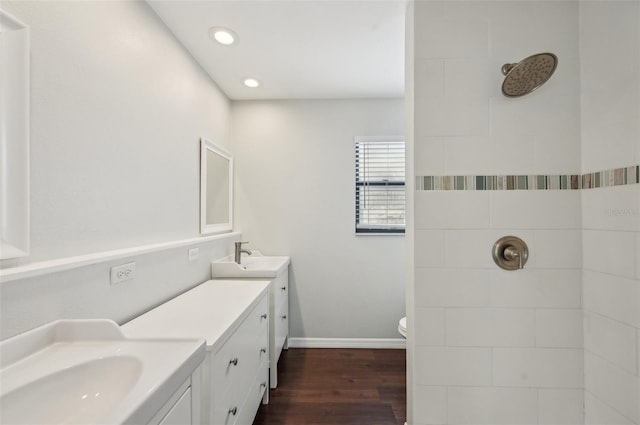 full bath with a sink, wood finished floors, tiled shower, double vanity, and baseboards